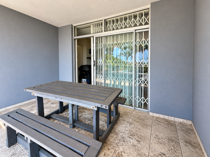 A covered patio area featuring tiled flooring, a sliding glass door with a security gate, and a skylight, providing a functional outdoor living space.