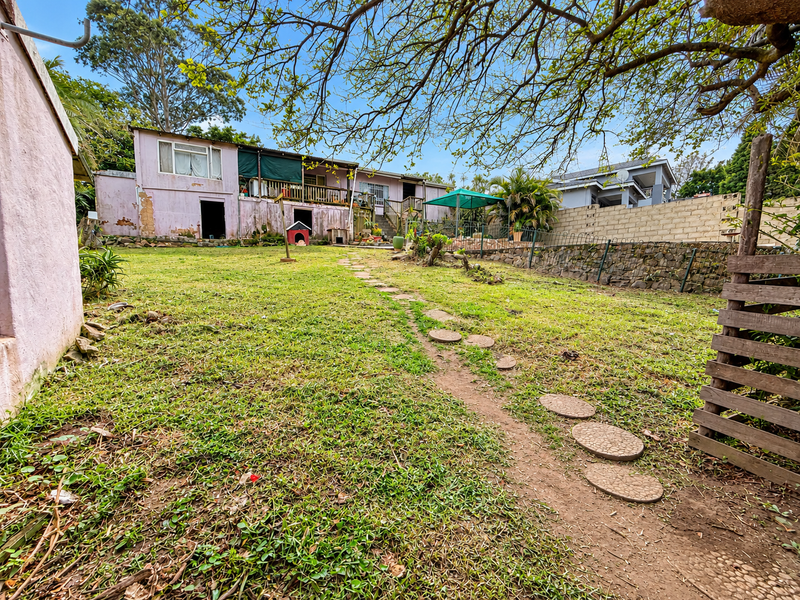 Spacious rear garden featuring a stone retaining wall, a raised timber deck, and a concrete block boundary wall, offering potential for landscaping improvements.