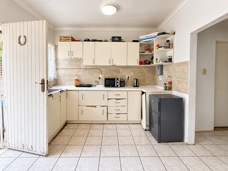 A functional kitchen featuring tiled flooring, a tiled backsplash, and built-in cabinetry, currently showing signs of wear and requiring cosmetic updates.