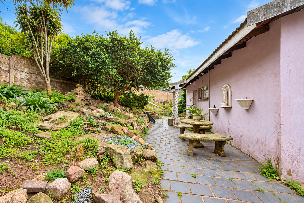 A rear exterior view featuring a paved walkway alongside a landscaped garden with stone features and a pink exterior wall with decorative wall mounts.