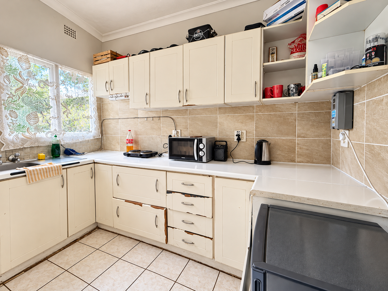 A functional kitchen featuring tiled backsplash, laminate cabinetry, and tiled flooring, currently showing signs of wear on the cabinet and drawer finishes.