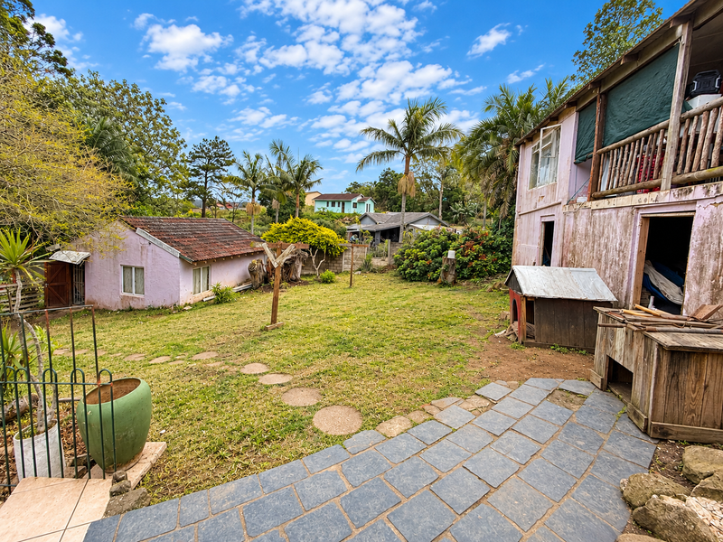 Spacious rear garden featuring a stone-paved patio, a detached outbuilding, and a multi-level dwelling with a timber balcony, set within a mature landscape.