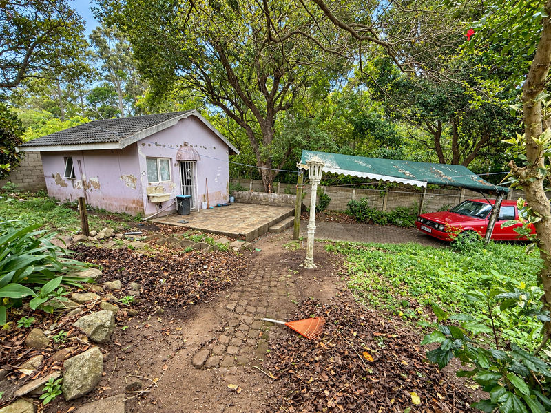 Rear view of the property featuring a paved patio area, external sink, and a detached structure with weathered exterior finishes and mature garden surroundings.
