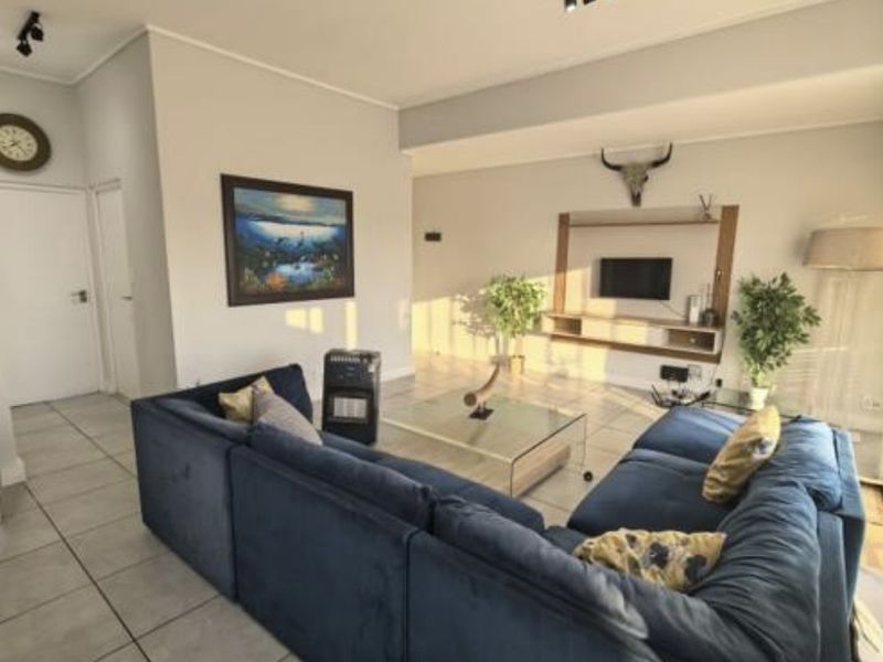 Spacious living room featuring neutral tiled flooring, modern recessed track lighting, and a built-in media console unit.