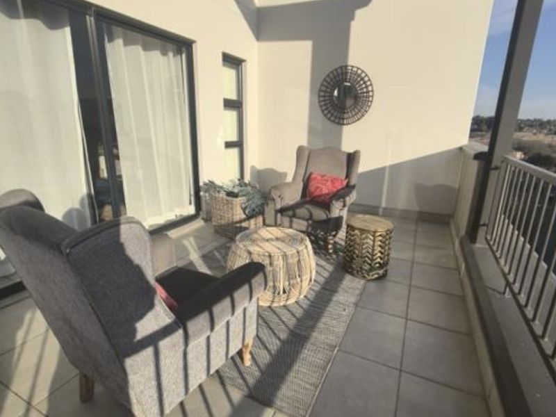 A modern covered balcony featuring tiled flooring, a metal balustrade, and large sliding glass doors providing access to the interior.