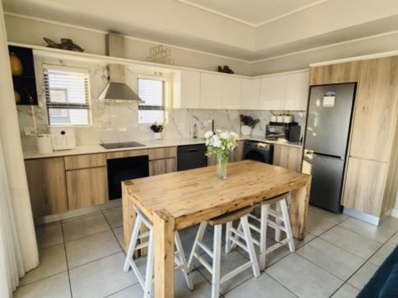 Modern kitchen featuring wood-tone and white cabinetry, stone countertops, integrated appliances, and tiled flooring, complemented by contemporary track lighting.