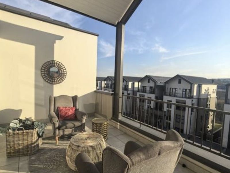 A spacious covered balcony featuring tiled flooring and a metal balustrade, offering an elevated view of the surrounding residential complex.