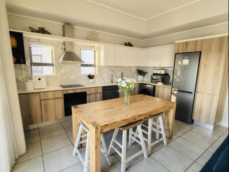 Modern open-plan kitchen featuring wood-grain and white cabinetry, marble-look backsplash, built-in appliances, and tiled flooring, seamlessly integrated with the living area.