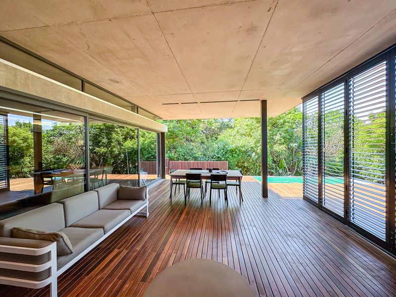 Spacious covered patio featuring high-quality timber decking, concrete ceiling, and large sliding glass doors that open to a lush garden and pool area.