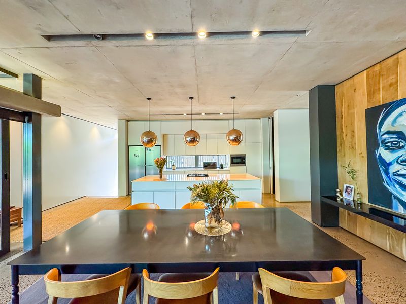 Modern open-plan living and dining area featuring a sleek kitchen island, exposed concrete ceilings, and high-end integrated appliances.