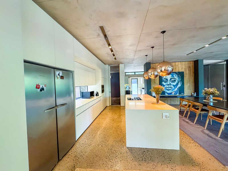 Modern open-plan kitchen featuring a large central island, sleek white cabinetry, polished concrete floors, and exposed concrete ceilings with contemporary pendant lighting.