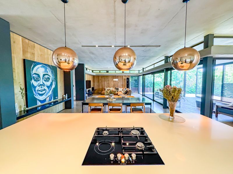 Spacious open-plan living area featuring a modern kitchen island with integrated gas cooktop, exposed concrete ceilings, and seamless flow to the outdoor deck.