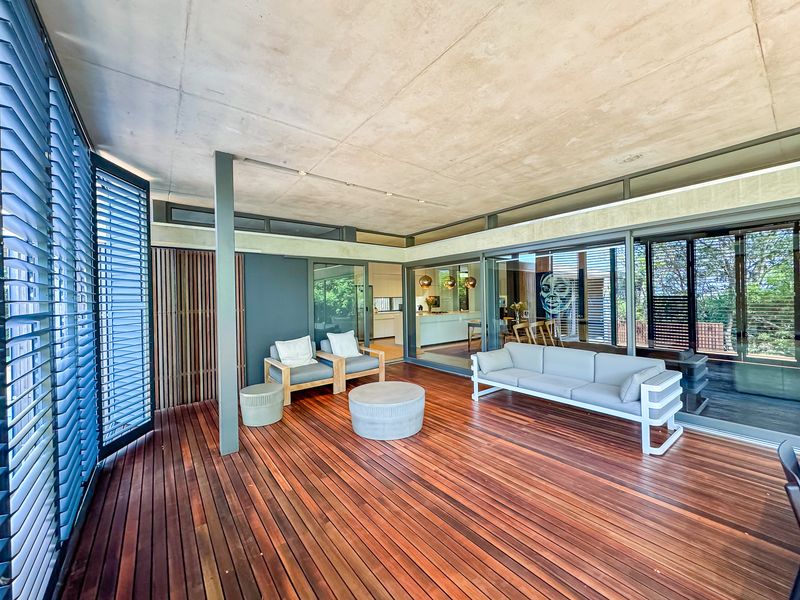 A spacious covered patio featuring high-quality timber decking, a raw concrete ceiling, and large sliding glass doors that provide seamless indoor-outdoor flow.