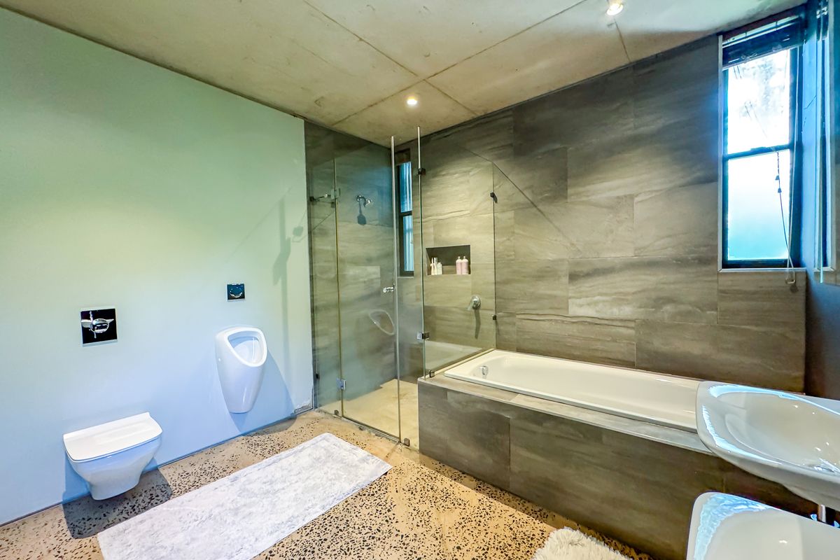 Modern bathroom featuring a wall-mounted toilet, urinal, glass-enclosed shower, and a built-in bathtub with contemporary tiled finishes and polished concrete flooring.