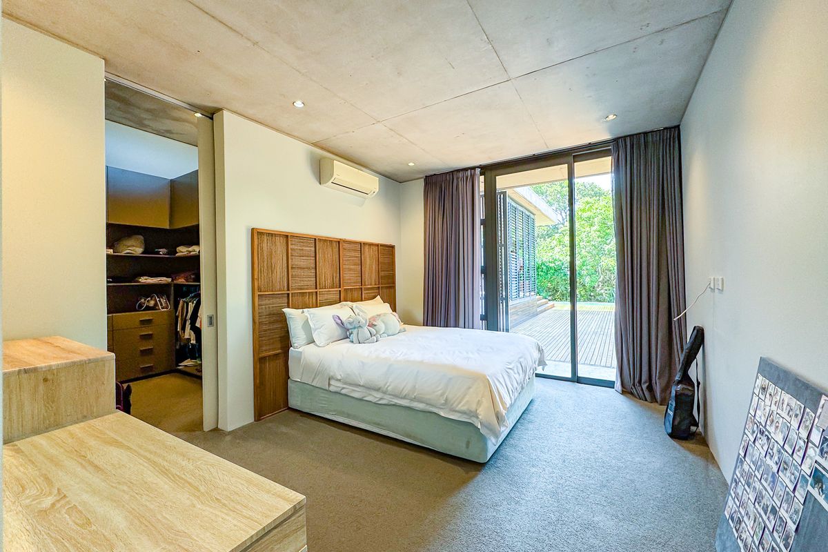 Modern bedroom featuring an exposed concrete ceiling, walk-in closet, and large sliding glass doors opening to an outdoor deck area.