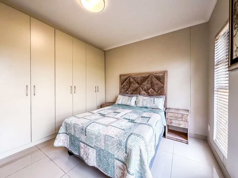 A well-maintained bedroom featuring extensive built-in cupboards, neutral tiled flooring, and natural light provided by a window with fitted venetian blinds.