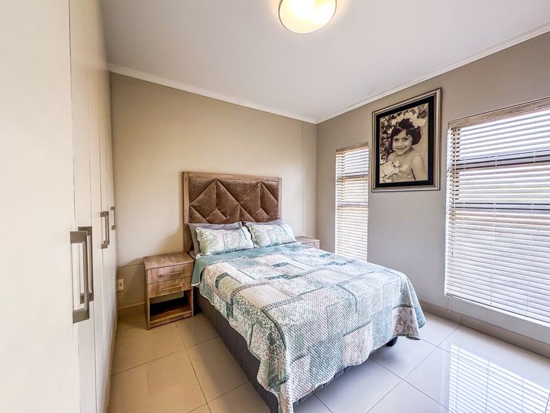 A well-maintained bedroom featuring neutral tiled flooring, built-in cupboards, and large windows fitted with venetian blinds for natural light control.