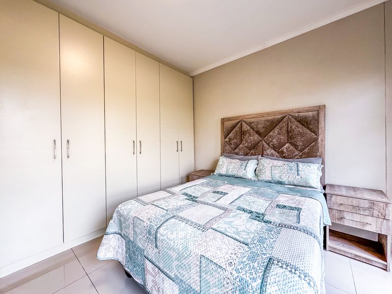A well-maintained bedroom featuring neutral tiled flooring, ample built-in cupboard storage, and clean wall finishes.