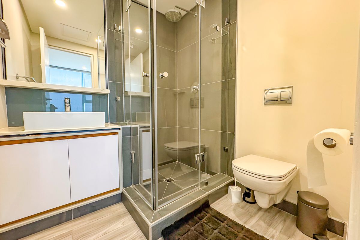 Modern bathroom featuring a glass-enclosed shower, wall-mounted toilet, and a sleek vanity with a vessel sink, finished with contemporary tiling.