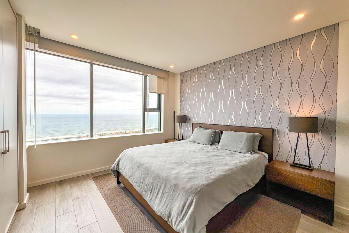A modern bedroom featuring large floor-to-ceiling windows with expansive ocean views, built-in wardrobe, and contemporary finishes.