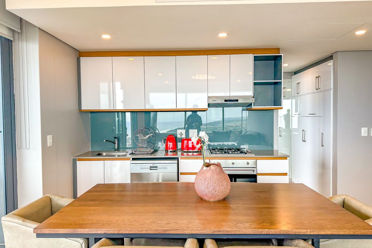 Modern kitchen featuring high-gloss cabinetry, integrated appliances, gas hob, and a sleek glass splashback, seamlessly integrated into an open-plan living space.