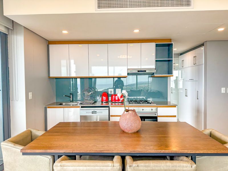 Modern kitchen featuring high-gloss cabinetry, integrated appliances, gas hob, and a sleek glass splashback, seamlessly integrated into an open-plan living space.