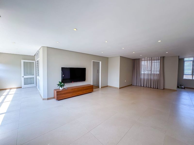 Spacious and bright open-plan living area featuring neutral tiled flooring, recessed downlighting, and clean finishes throughout.