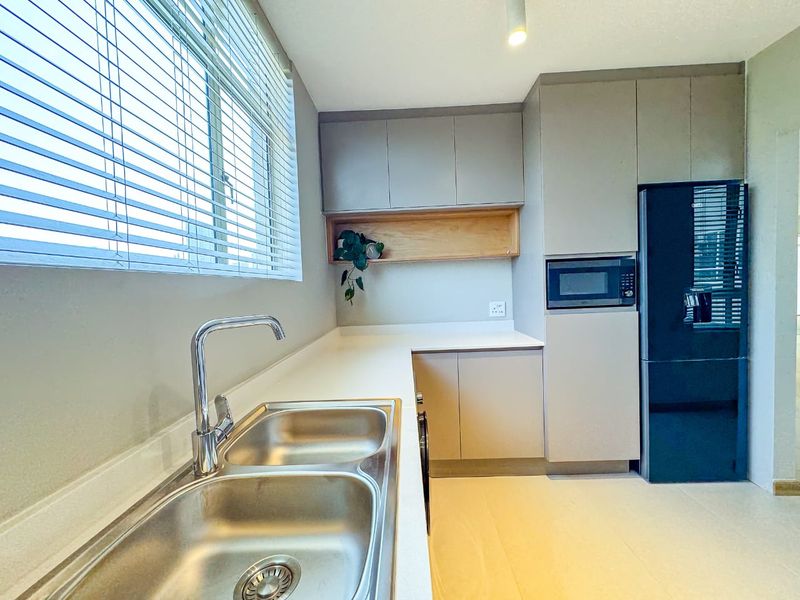 Modern kitchen featuring sleek cabinetry, a double bowl stainless steel sink with chrome mixer tap, and integrated microwave, offering a clean and functional workspace.