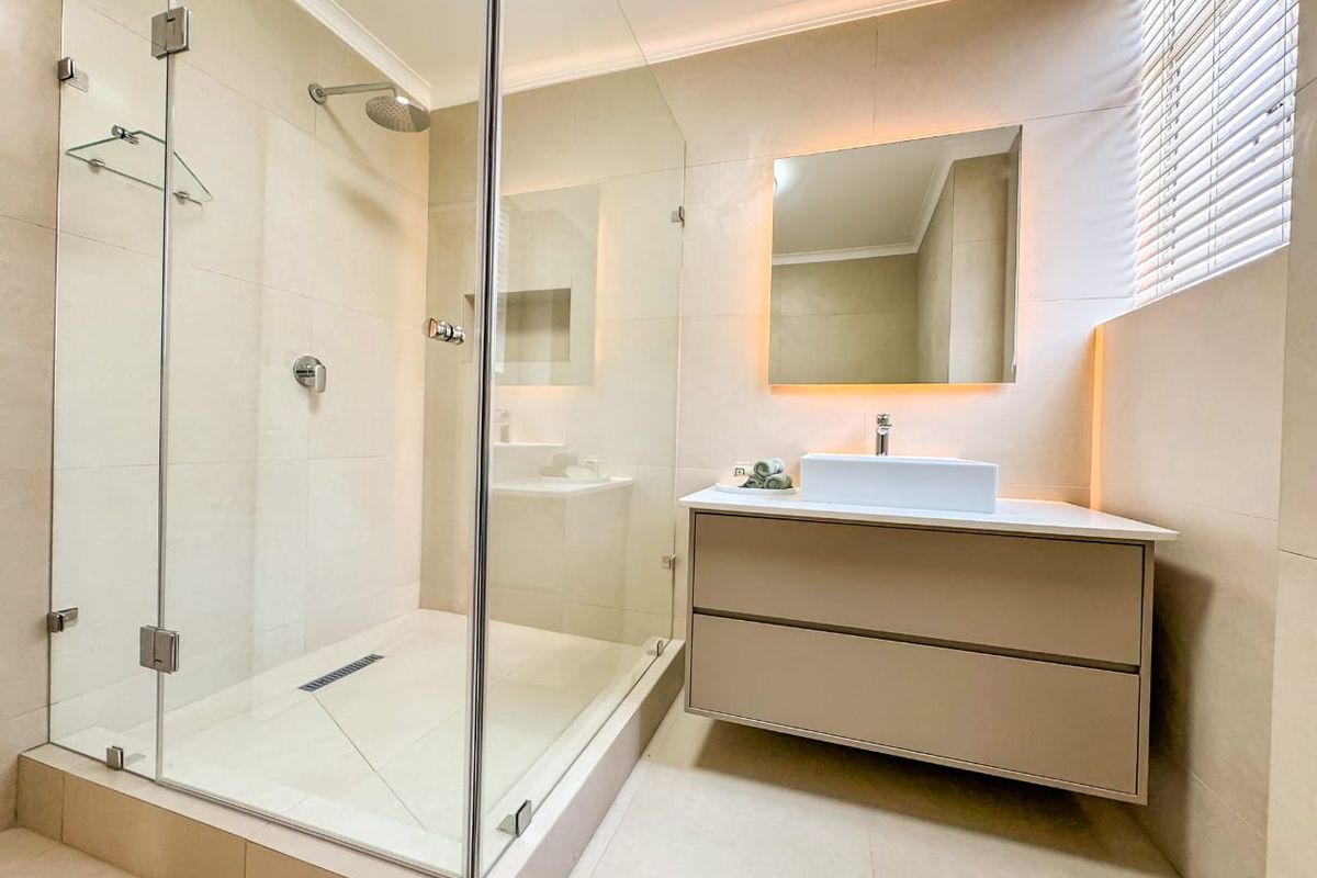 Modern bathroom featuring a spacious walk-in shower with glass enclosure, a sleek floating vanity with basin, and elegant backlit mirror lighting.