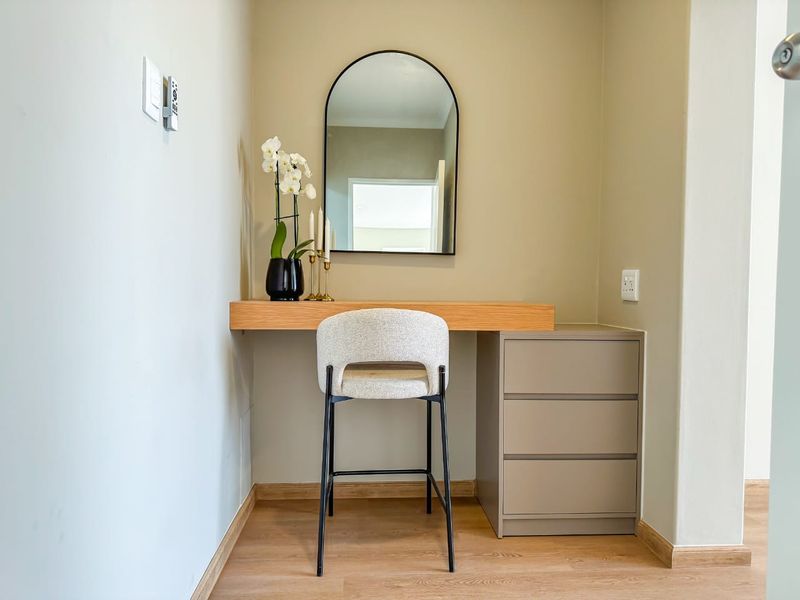 A compact bedroom nook featuring a modern built-in floating desk, integrated drawer storage, and light wood-look laminate flooring.