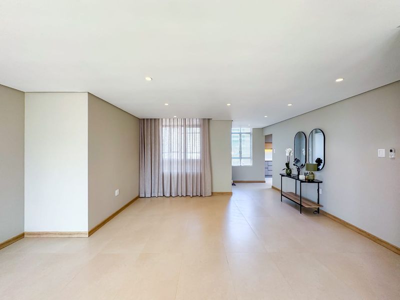 Spacious open-plan living area featuring neutral tiled flooring, recessed downlighting, and large windows with fitted blinds, offering a bright and modern blank canvas.