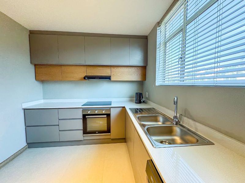 Modern kitchen featuring sleek grey and wood-tone cabinetry, stone countertops, integrated electric hob, oven, extractor fan, and a double stainless steel sink.