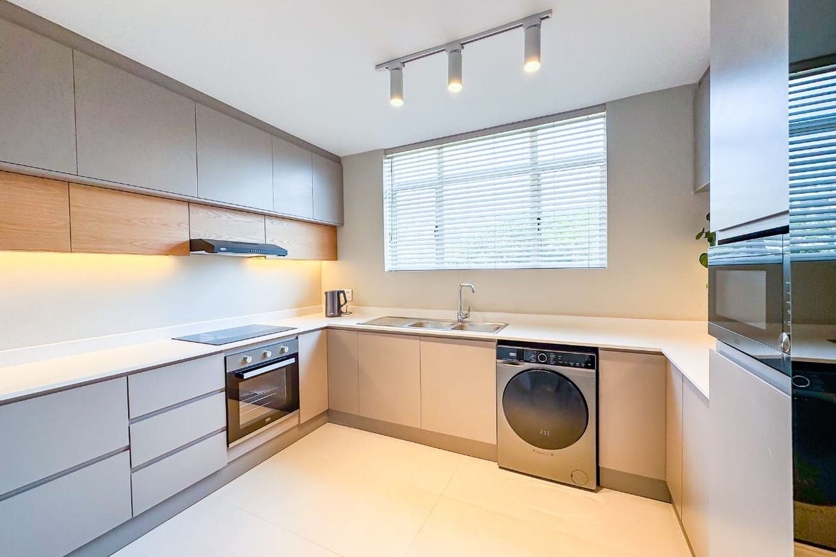 Modern kitchen featuring sleek handleless cabinetry, stone countertops, integrated oven, electric hob, and high-quality finishes with ample natural light.