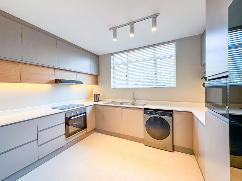 Modern kitchen featuring sleek handleless cabinetry, stone countertops, integrated oven, electric hob, and high-quality finishes with ample natural light.
