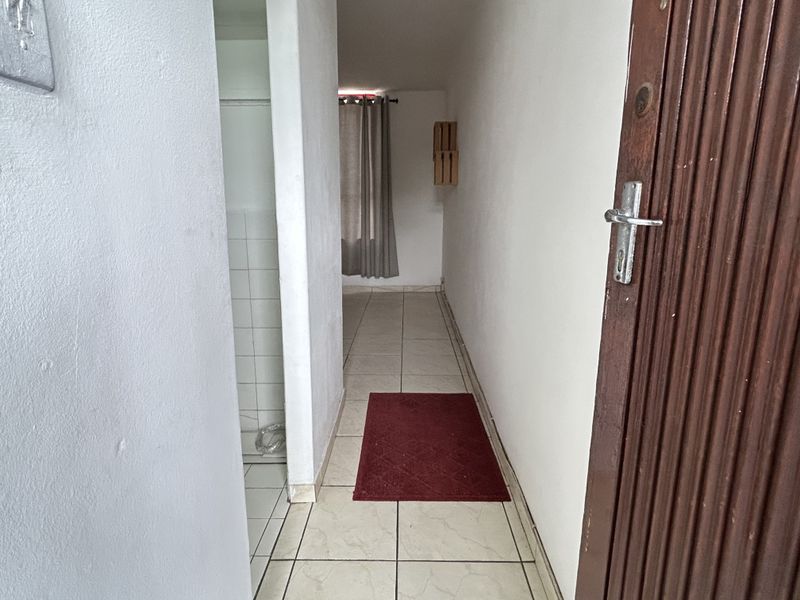 A narrow interior hallway featuring tiled flooring and neutral wall finishes, leading towards a secondary space with a window.