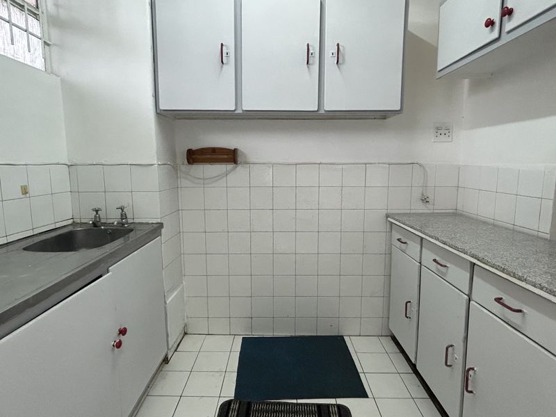 A functional kitchen space featuring white built-in cabinetry, a stainless steel sink, and tiled finishes, offering a blank canvas for modern renovation.