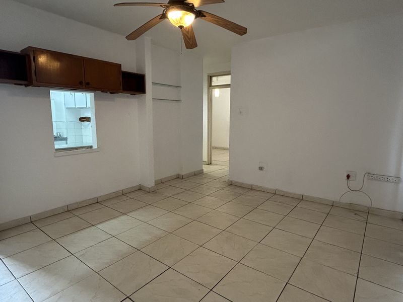 An empty living room featuring tiled flooring, a ceiling fan, and a convenient pass-through window connecting to the kitchen area.