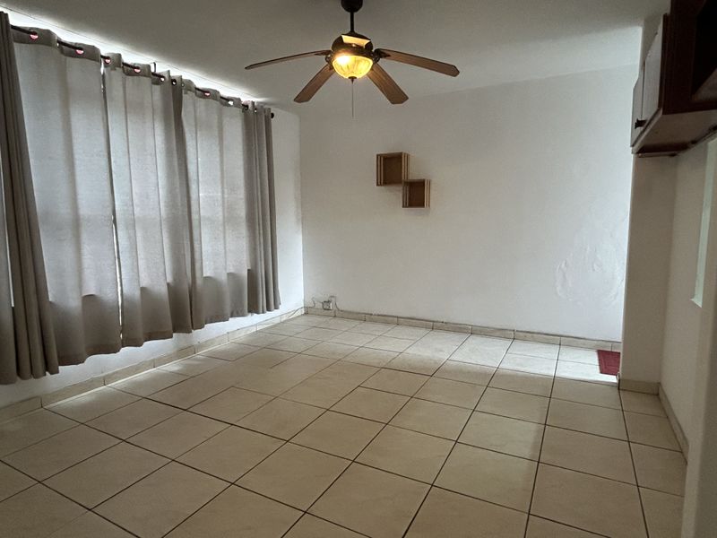 An empty living room featuring ceramic floor tiles, a ceiling fan, and neutral wall finishes, offering a blank canvas for personalization.