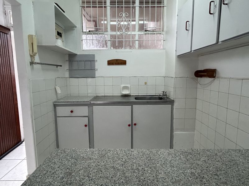 A compact kitchen featuring built-in cabinetry, a stainless steel sink, granite countertops, and tiled walls, offering a functional space ready for modernization.