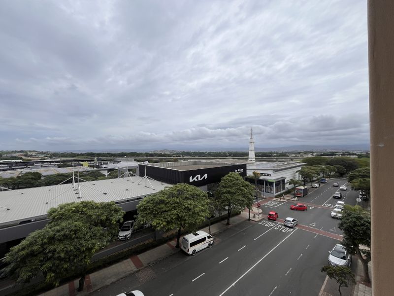 Elevated urban view overlooking a commercial street, nearby retail buildings, and surrounding landscape under a cloudy sky.