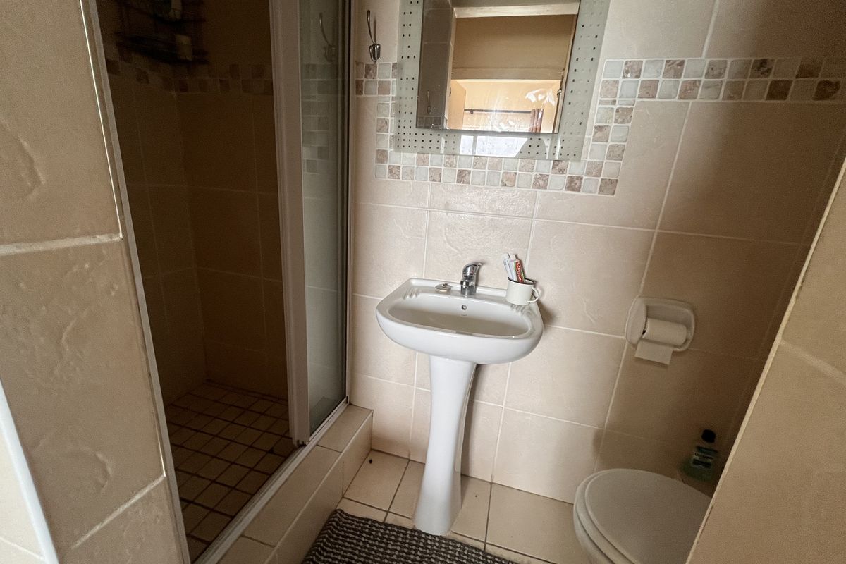 A compact bathroom featuring a pedestal basin, a shower enclosure, and neutral wall tiling with decorative mosaic accents.