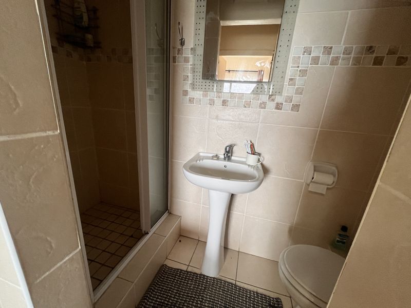 A compact bathroom featuring a pedestal basin, a shower enclosure, and neutral wall tiling with decorative mosaic accents.