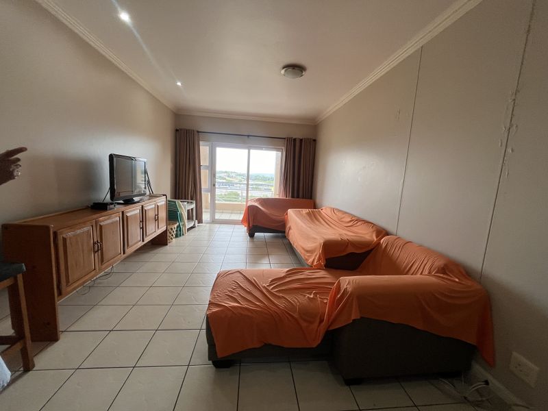 A spacious living room featuring tiled flooring, recessed lighting, and a sliding glass door that provides access to an outdoor balcony area.