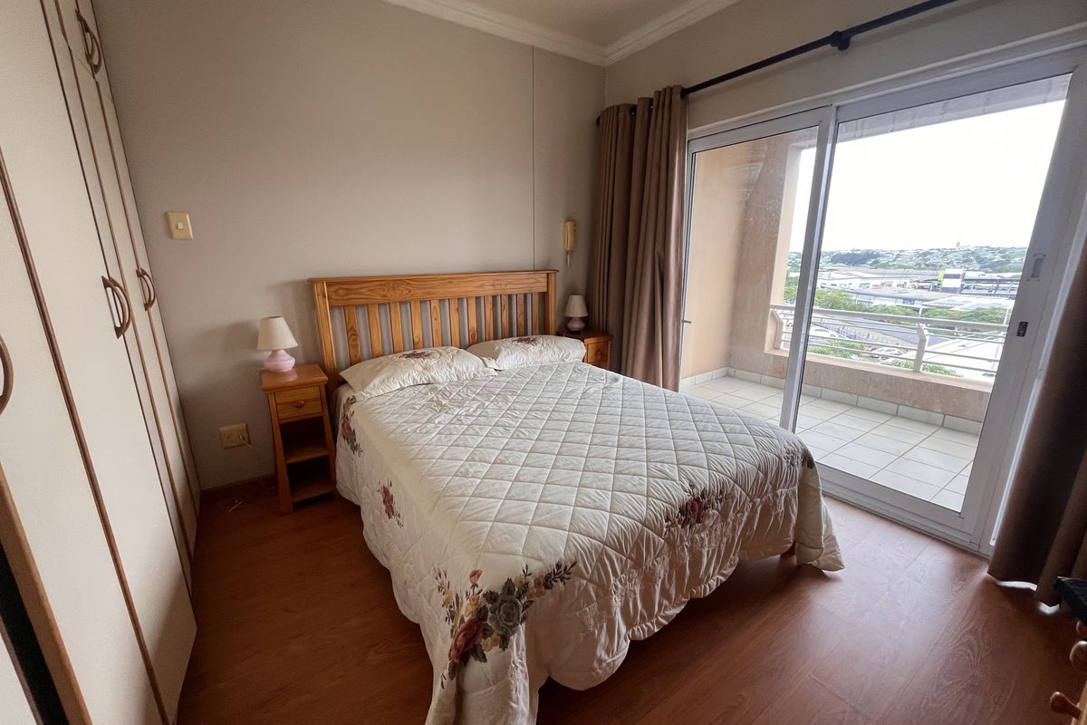 A bedroom featuring laminate flooring, built-in cupboards, and a sliding glass door providing direct access to a private balcony with an elevated view.