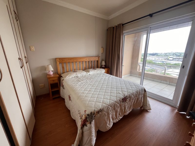 A bedroom featuring laminate flooring, built-in cupboards, and a sliding glass door providing direct access to a private balcony with an elevated view.
