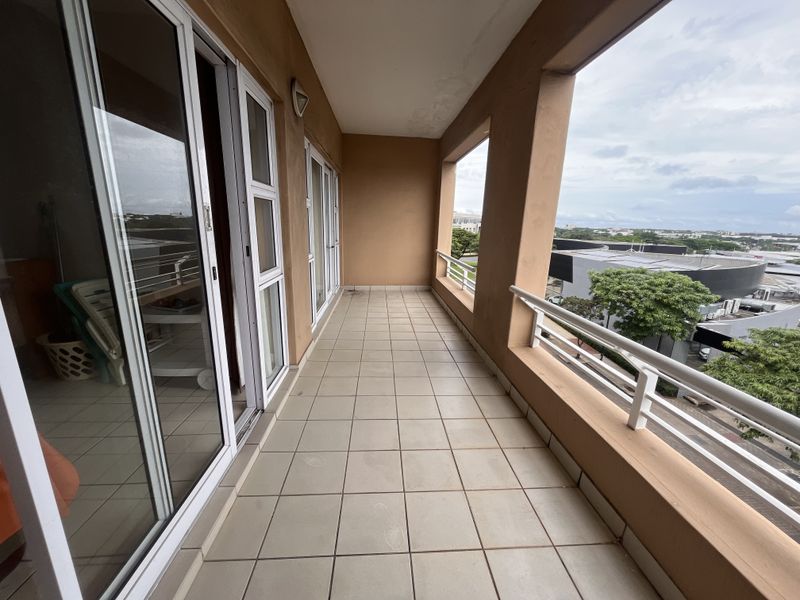 A spacious covered balcony featuring tiled flooring, sliding glass door access, and a metal balustrade with views of the surrounding area.