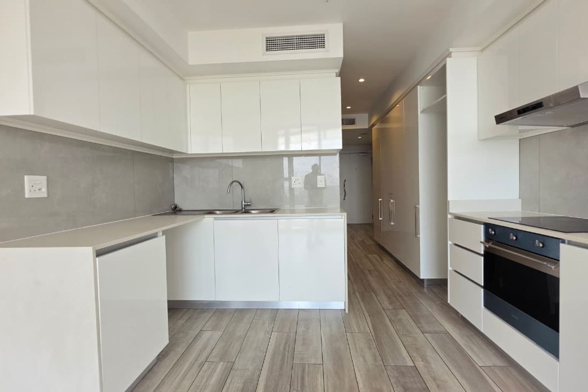 Modern, minimalist kitchen featuring sleek white cabinetry, integrated appliances, a stainless steel sink, and contemporary tiled flooring in an open-plan layout.