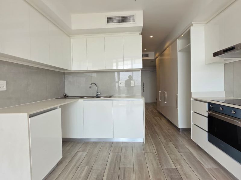 Modern, minimalist kitchen featuring sleek white cabinetry, integrated appliances, a stainless steel sink, and contemporary tiled flooring in an open-plan layout.