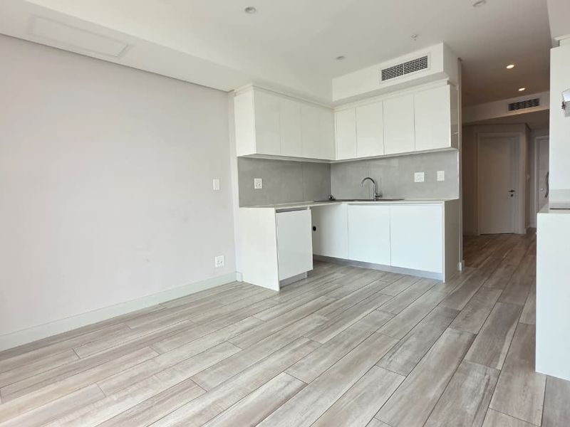 Modern open-plan kitchen and living area featuring sleek white cabinetry, integrated appliances, recessed lighting, and contemporary wood-look tiled flooring throughout.