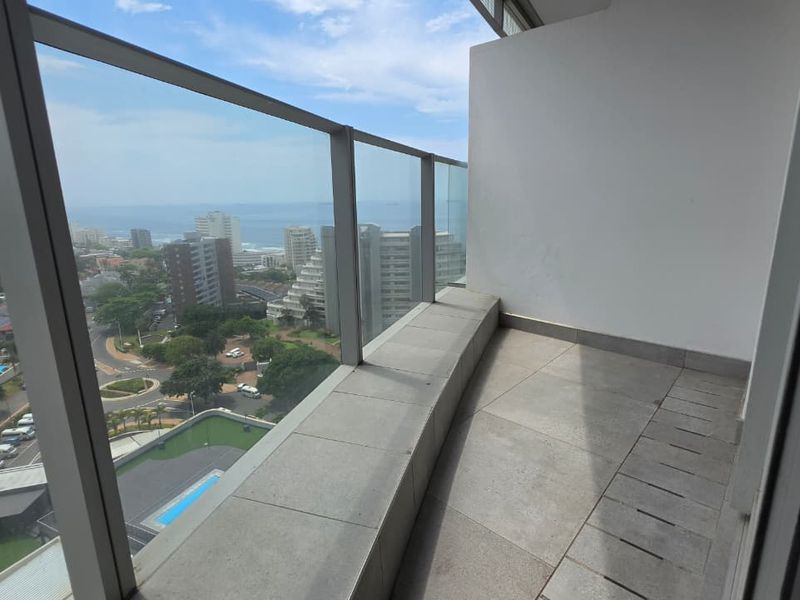 A modern balcony featuring a glass balustrade and tiled flooring, offering elevated views of the surrounding urban landscape and coastline.